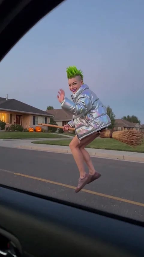 The My Ride Is Here broom trend made from one photo: a woman with a lime-green mohawk rides a broomstick outside a car window at dusk